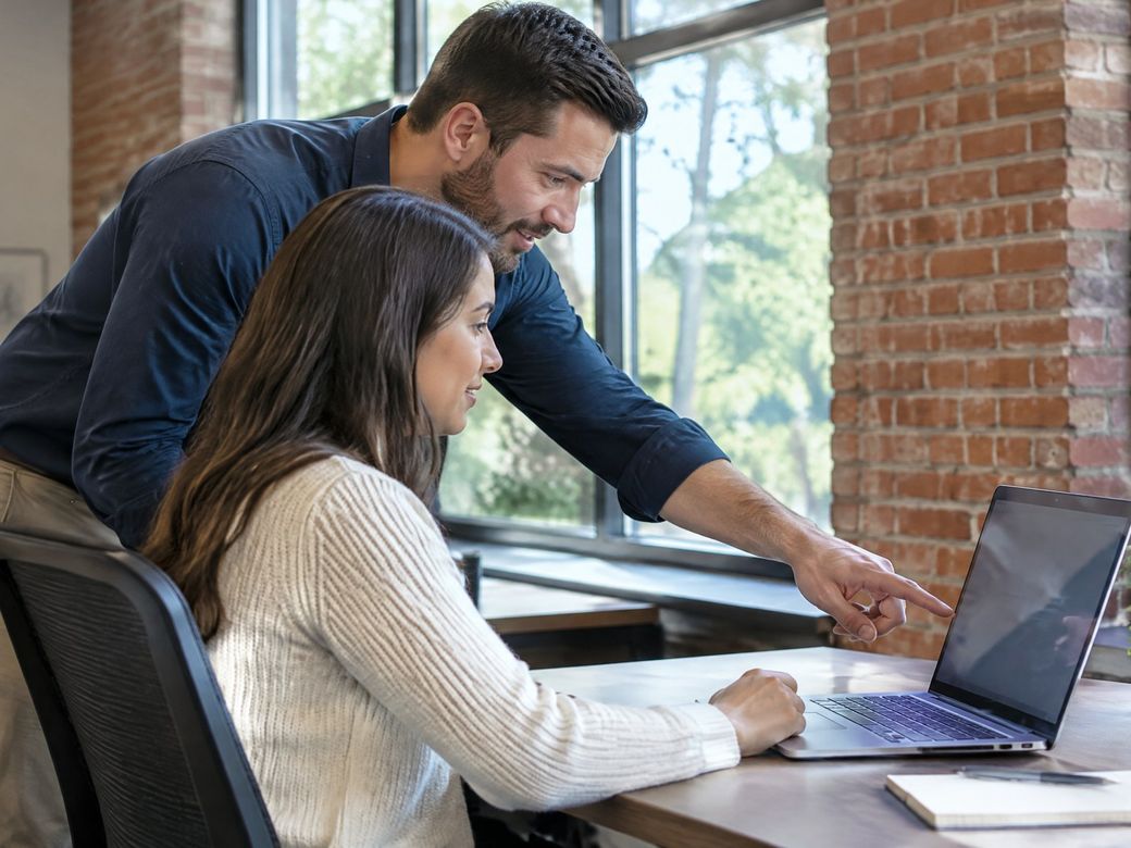 IT technician helping an employee with her laptop in a bright office with a brick wall and large windows