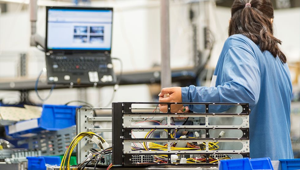 Technician wiring a computer chassis at a hardware workbench with a laptop nearby